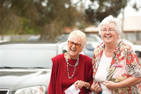 Two grey haired women smile at the camera.